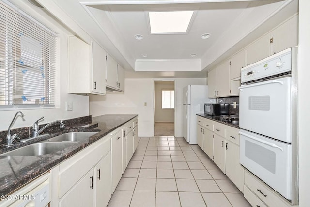 kitchen with white appliances, light tile patterned floors, a sink, white cabinets, and a raised ceiling