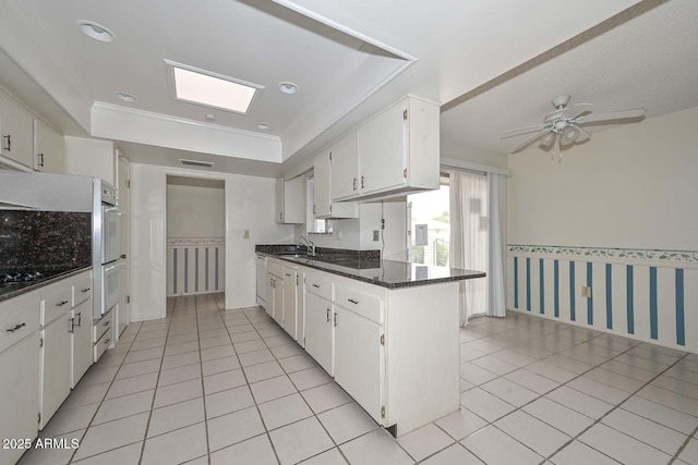 kitchen featuring a sink, white cabinetry, a peninsula, light tile patterned flooring, and wallpapered walls