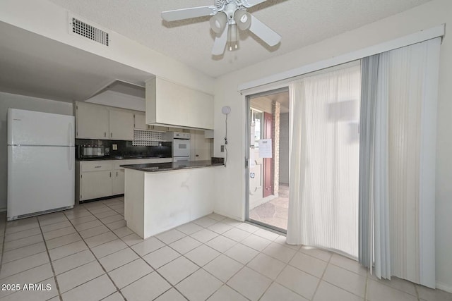 kitchen with dark countertops, visible vents, ceiling fan, a peninsula, and freestanding refrigerator