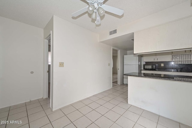 kitchen featuring light tile patterned floors, visible vents, freestanding refrigerator, ceiling fan, and black microwave