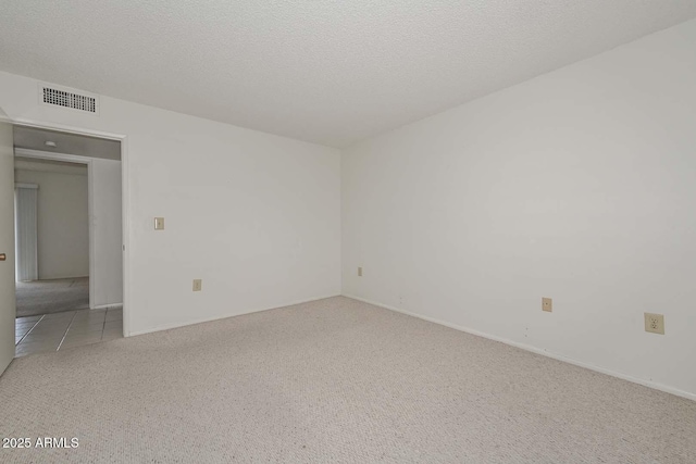 carpeted empty room with tile patterned floors, visible vents, and a textured ceiling