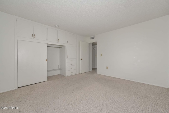 unfurnished bedroom featuring light colored carpet, visible vents, a closet, and a textured ceiling