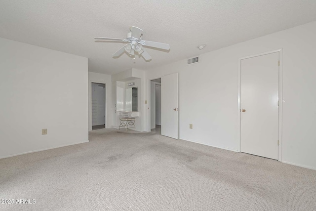 unfurnished bedroom featuring visible vents, light colored carpet, a textured ceiling, and a ceiling fan