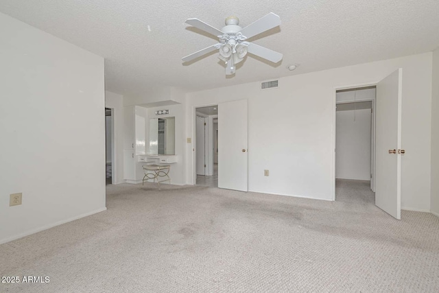 unfurnished bedroom with a spacious closet, visible vents, ceiling fan, carpet floors, and a textured ceiling