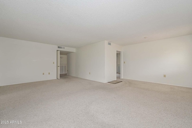 empty room featuring visible vents, light colored carpet, and a textured ceiling