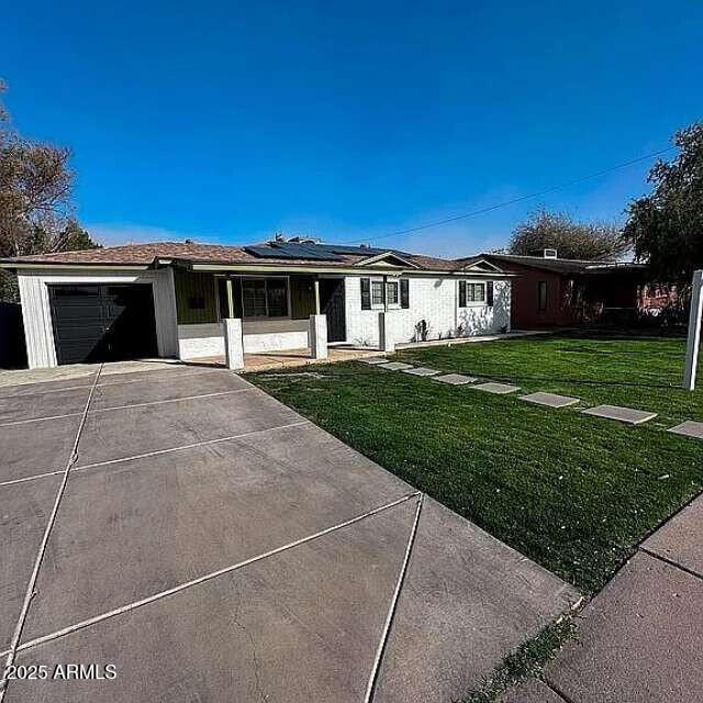 ranch-style home featuring a front yard, concrete driveway, a garage, and roof mounted solar panels