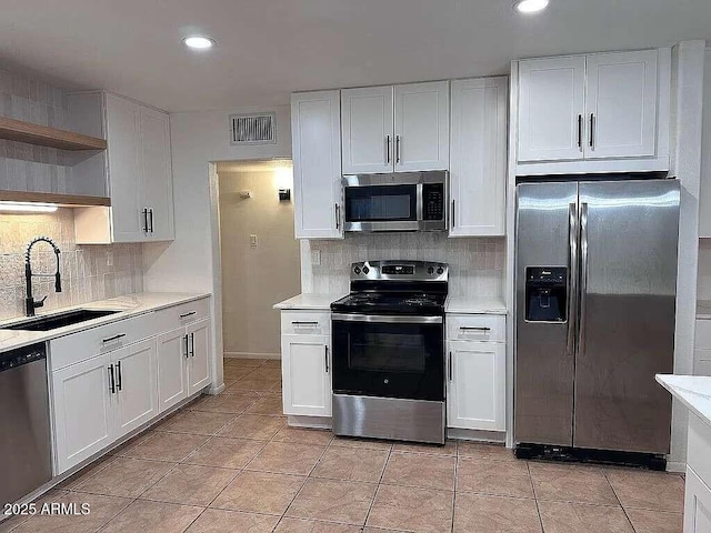 kitchen featuring visible vents, a sink, open shelves, appliances with stainless steel finishes, and light countertops