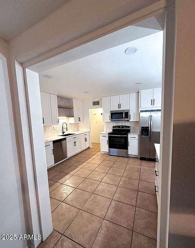kitchen featuring backsplash, white cabinetry, stainless steel appliances, and a sink