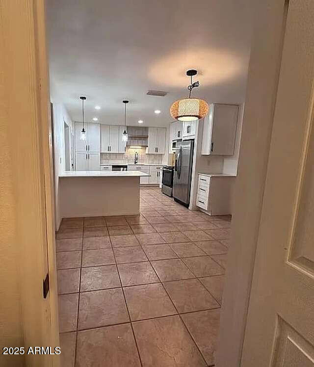 kitchen with appliances with stainless steel finishes, a peninsula, light tile patterned flooring, light countertops, and hanging light fixtures