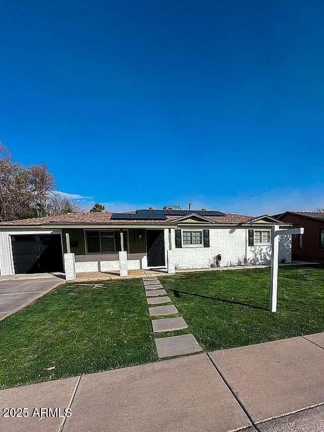 view of front facade featuring roof mounted solar panels, an attached garage, driveway, and a front lawn