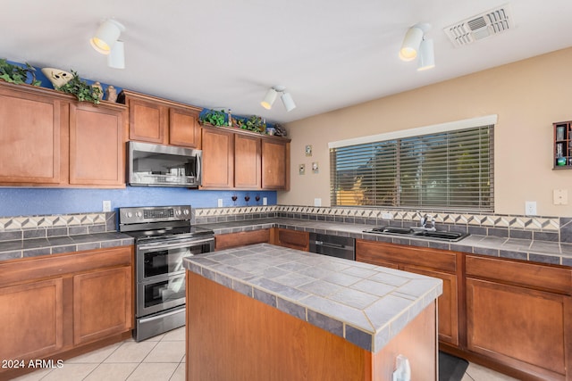 kitchen featuring tile countertops, sink, light tile patterned floors, a kitchen island, and appliances with stainless steel finishes