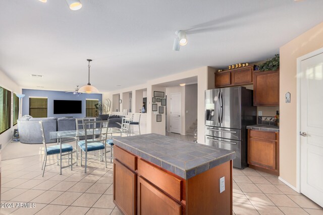 kitchen featuring light tile patterned flooring, stainless steel refrigerator with ice dispenser, ceiling fan, a center island, and pendant lighting