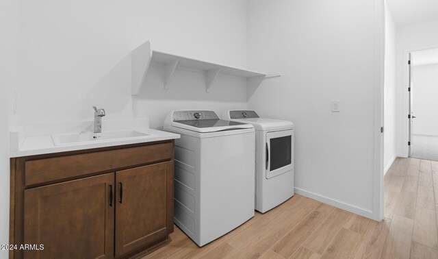 clothes washing area with separate washer and dryer, light hardwood / wood-style floors, and sink