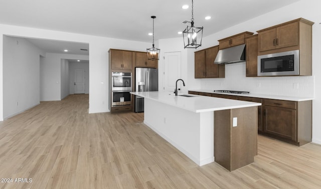 kitchen with a sink, light wood-style flooring, under cabinet range hood, stainless steel appliances, and a kitchen island with sink