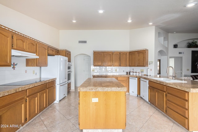 kitchen with a high ceiling, backsplash, white appliances, sink, and a center island