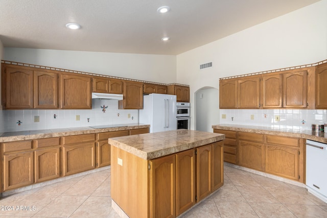 kitchen with backsplash, white appliances, a center island, and lofted ceiling