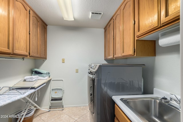 clothes washing area with washer and dryer, a textured ceiling, light tile flooring, and sink