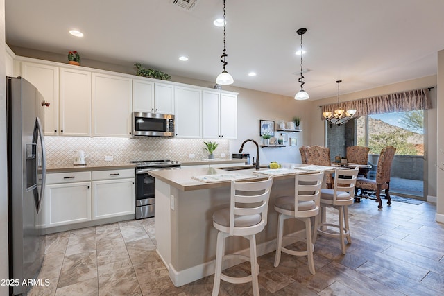 kitchen featuring white cabinetry, stainless steel appliances, hanging light fixtures, and an island with sink