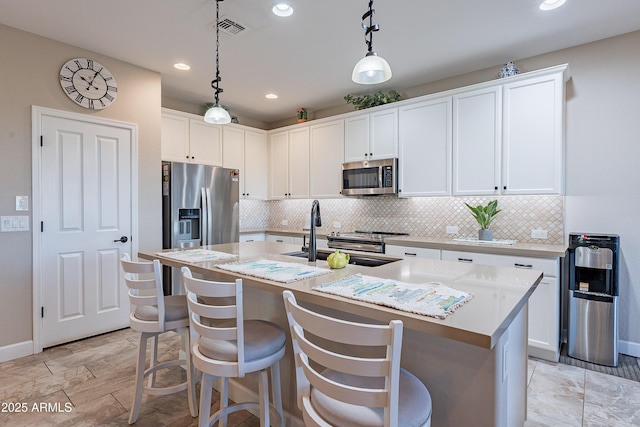 kitchen featuring stainless steel appliances, a kitchen island with sink, sink, decorative light fixtures, and white cabinetry