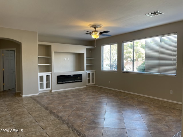 unfurnished living room featuring built in features, dark tile patterned floors, and ceiling fan