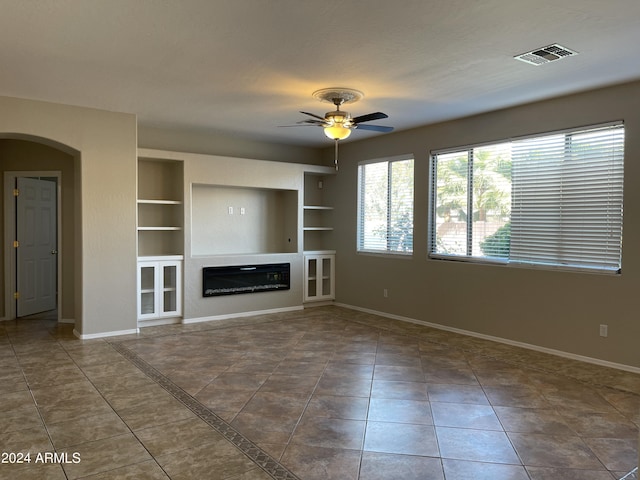 unfurnished living room with built in shelves, ceiling fan, and dark tile patterned floors