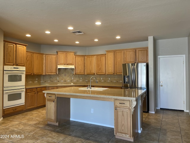 kitchen featuring stainless steel refrigerator with ice dispenser, a kitchen breakfast bar, white double oven, a kitchen island with sink, and sink