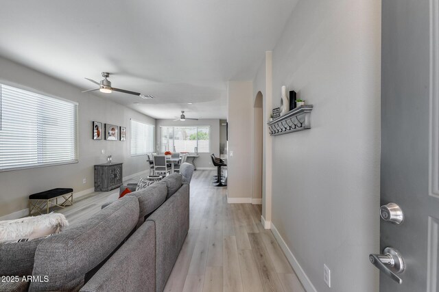 living area featuring light wood finished floors, arched walkways, baseboards, visible vents, and ceiling fan