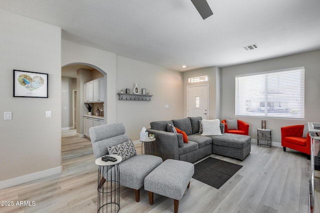 living area featuring visible vents, a ceiling fan, arched walkways, light wood-type flooring, and baseboards