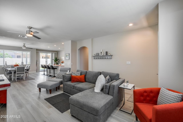living area featuring arched walkways, light wood-type flooring, visible vents, and a ceiling fan