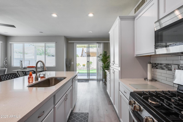 kitchen with recessed lighting, a sink, decorative backsplash, light wood-style flooring, and appliances with stainless steel finishes