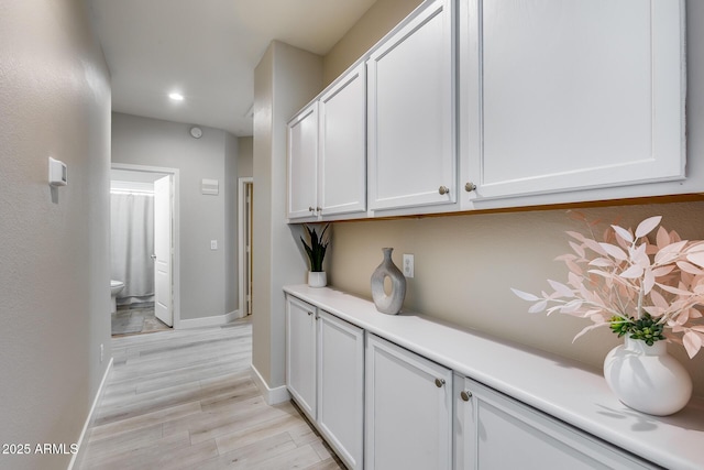 corridor featuring light wood-style flooring, baseboards, and recessed lighting
