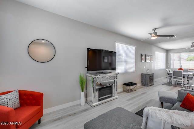 living room with ceiling fan, baseboards, a glass covered fireplace, and wood finished floors