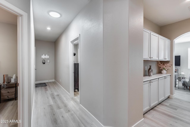 hall featuring arched walkways, light wood-style floors, and baseboards