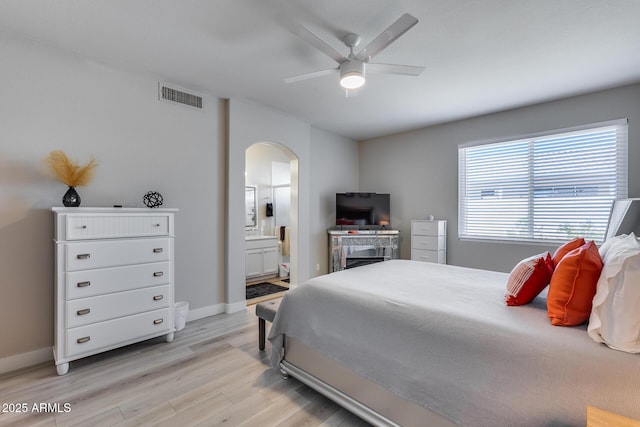 bedroom with light wood finished floors, visible vents, arched walkways, baseboards, and ensuite bathroom