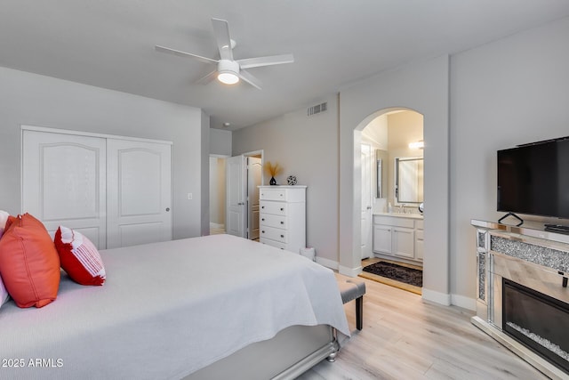 bedroom featuring light wood finished floors, visible vents, arched walkways, a closet, and ensuite bathroom