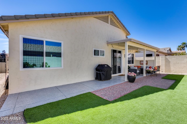 rear view of property with a lawn, a ceiling fan, fence, a patio, and stucco siding