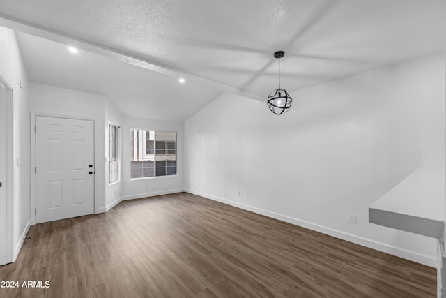 unfurnished dining area with a textured ceiling, vaulted ceiling with beams, and dark hardwood / wood-style floors