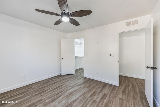 unfurnished bedroom featuring a walk in closet, ceiling fan, a closet, and hardwood / wood-style floors