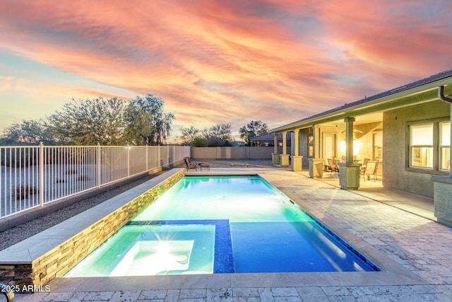 pool at dusk with an in ground hot tub and a patio