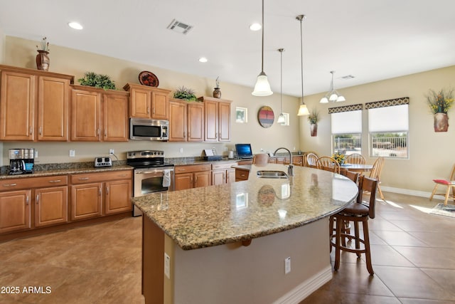 kitchen featuring a kitchen bar, decorative light fixtures, stainless steel appliances, sink, and a kitchen island with sink