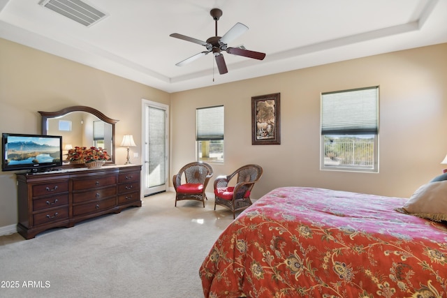 bedroom with ceiling fan, light colored carpet, and a tray ceiling