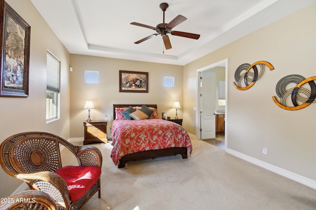 bedroom with ceiling fan, ensuite bath, light carpet, and a raised ceiling