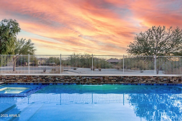 pool at dusk featuring an in ground hot tub