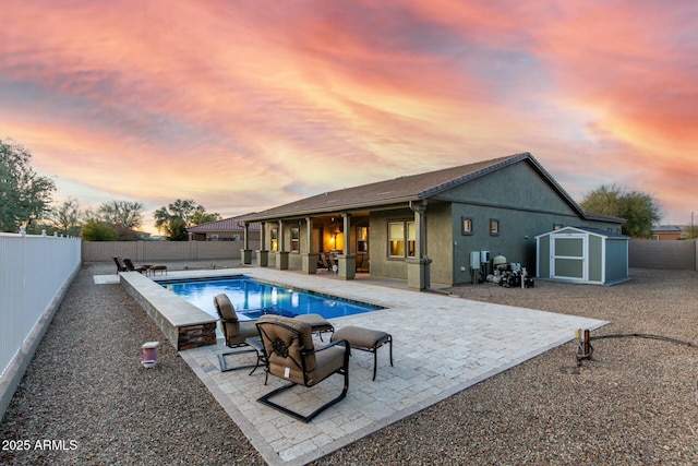 pool at dusk with a patio area and a shed