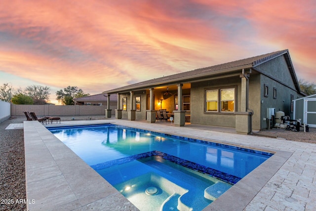 pool at dusk with an in ground hot tub and a patio area