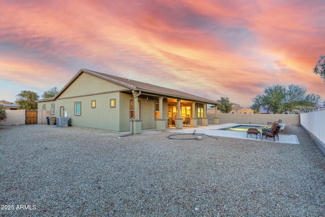 back house at dusk with cooling unit, a patio, and a fenced in pool