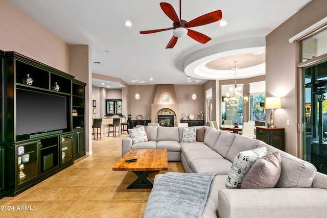 living room with a tray ceiling, a fireplace, light tile patterned floors, and ceiling fan with notable chandelier