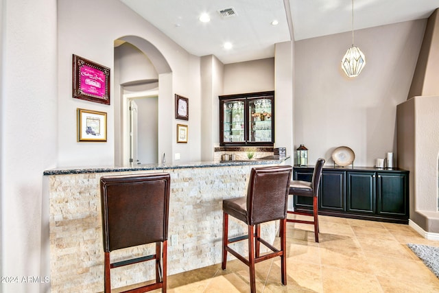 bar with stone countertops, light tile patterned floors, and hanging light fixtures