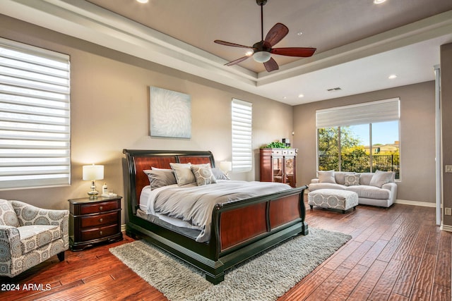 bedroom with ceiling fan, dark hardwood / wood-style flooring, and a tray ceiling