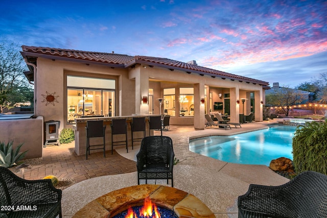 pool at dusk featuring an in ground hot tub, a bar, and a patio